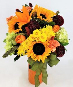 dark ruby dahlias with sunflowers and other orange and yellow flowers in a vase