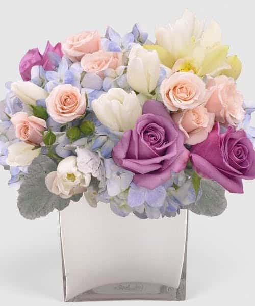 Featuring roses, tulips,and hydrangea in this remarkable arrangement is expertly crafted in soft Shades of Blue, pink and ivory. Choose The Premium Ceramic White keepsake pot for the most elegant style design.
