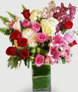 Elegance and Love is represented with shades of pink, red and white. This beautiful design features our leaf-wrapped signature clear vase. Pink, red and white lilies, roses, and hydrangea are nestled amongst other floral textures and finished with elegant greens. 